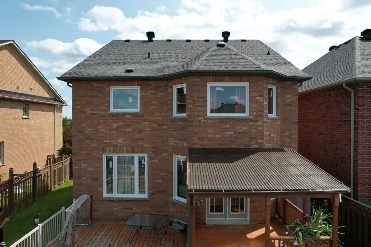 Rear of a two-storey brick GTA home with new white windows and garden doors opening onto a covered deck